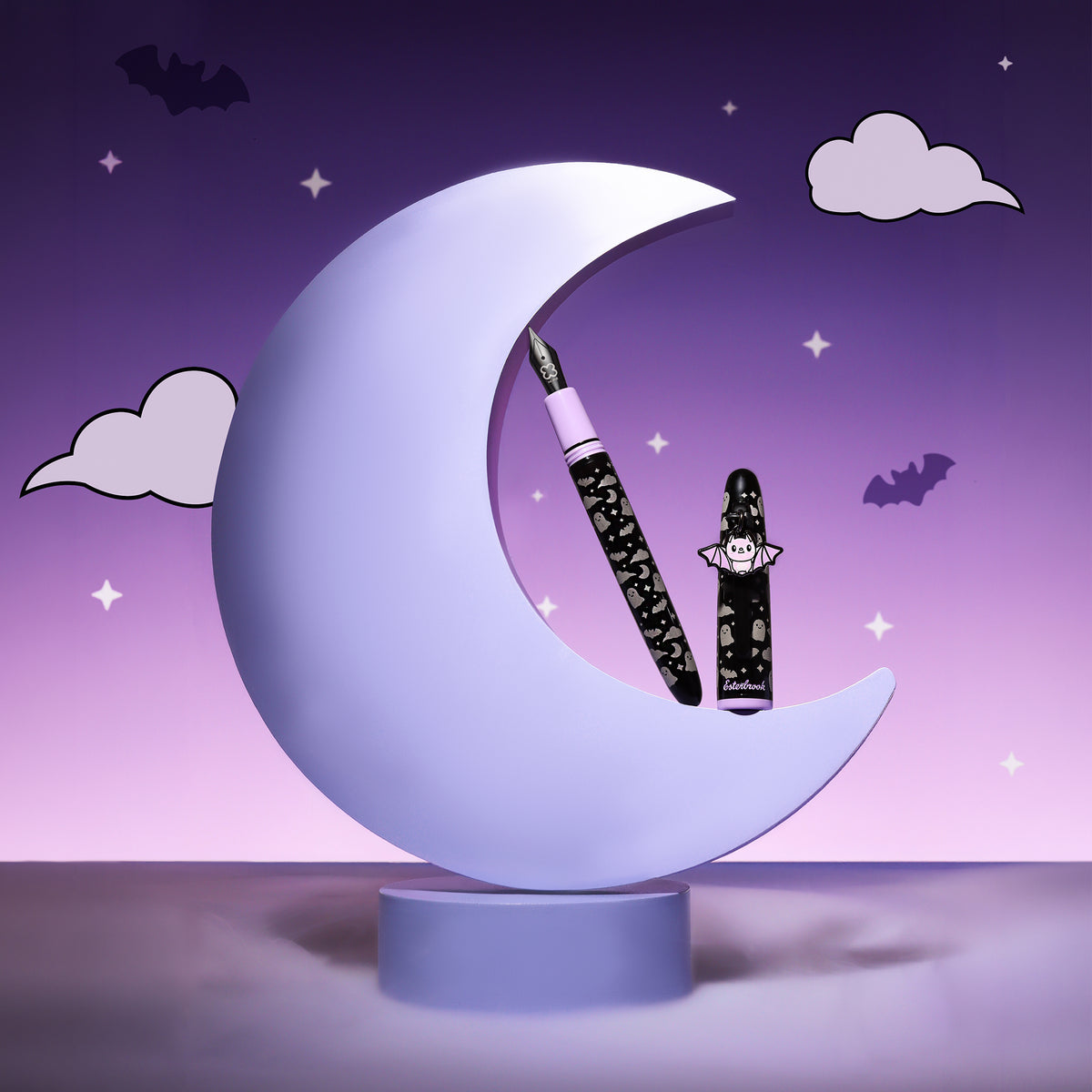 Esterbrook Sweetly Haunted Estie fountain pen, uncapped, with its cap and bat charm resting in a lavender crescent moon among bats, stars and clouds