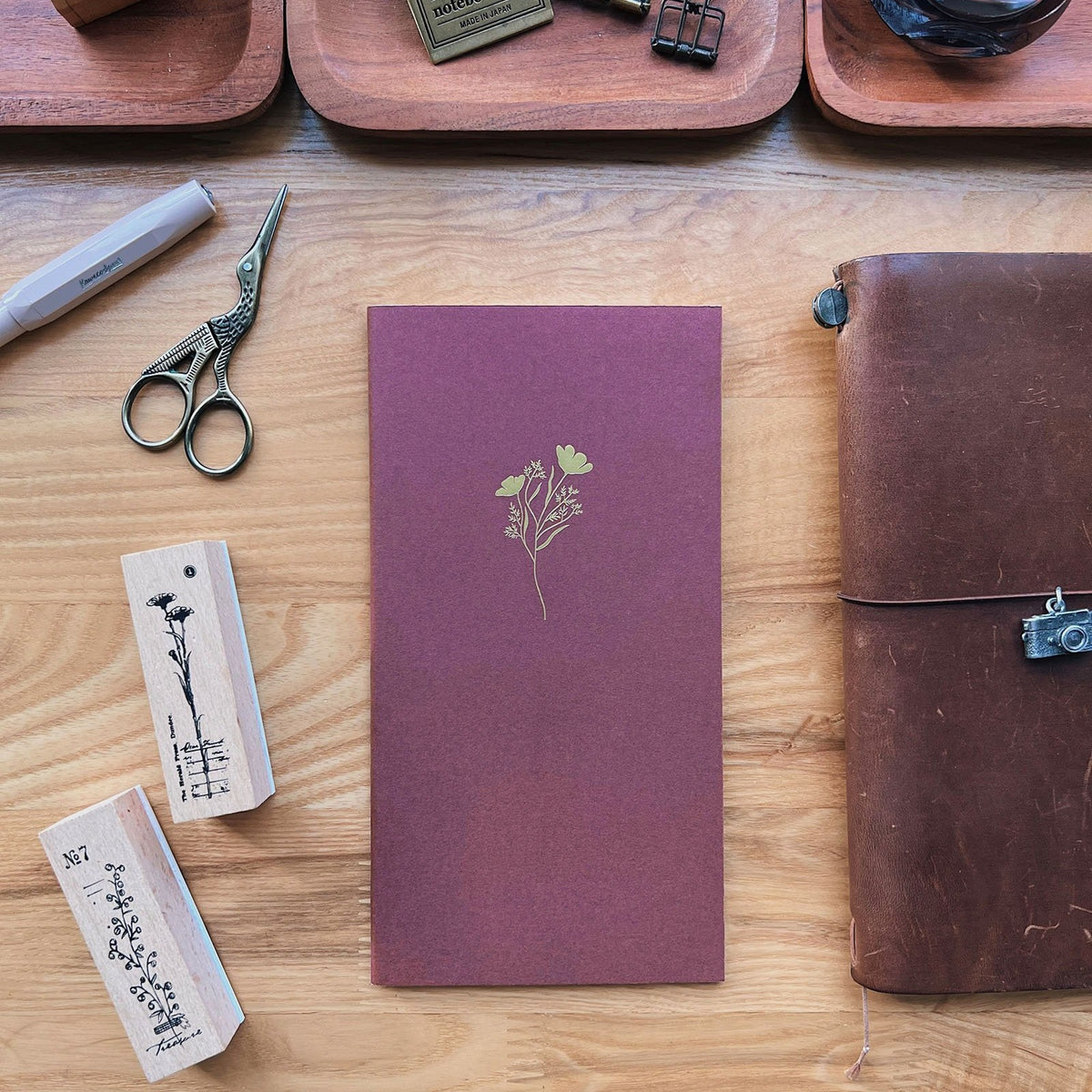 Sarica Studio Floral Notebook, standard TN size, bordeaux with a gold floral design, on a desk with floral rubber stamps