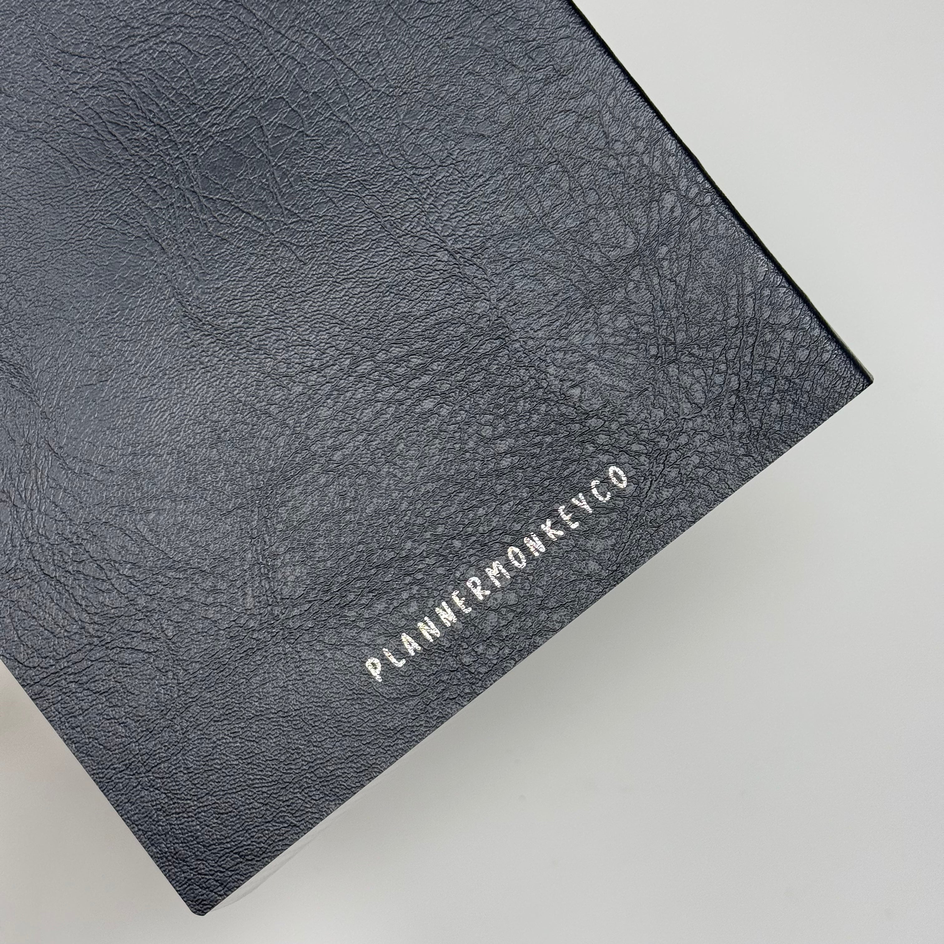 Close view of the black Freely Noted A5 notebook cover showing its pebbled texture and the Planner Monkey Co name debossed in silver