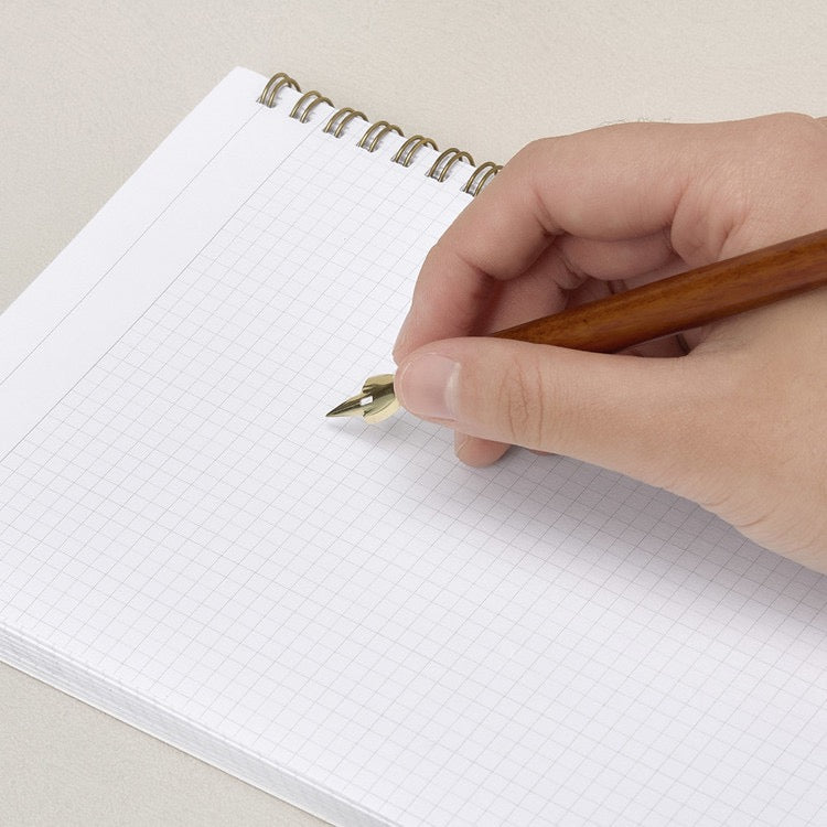 Hand holding wooden dip pen writing on white paper