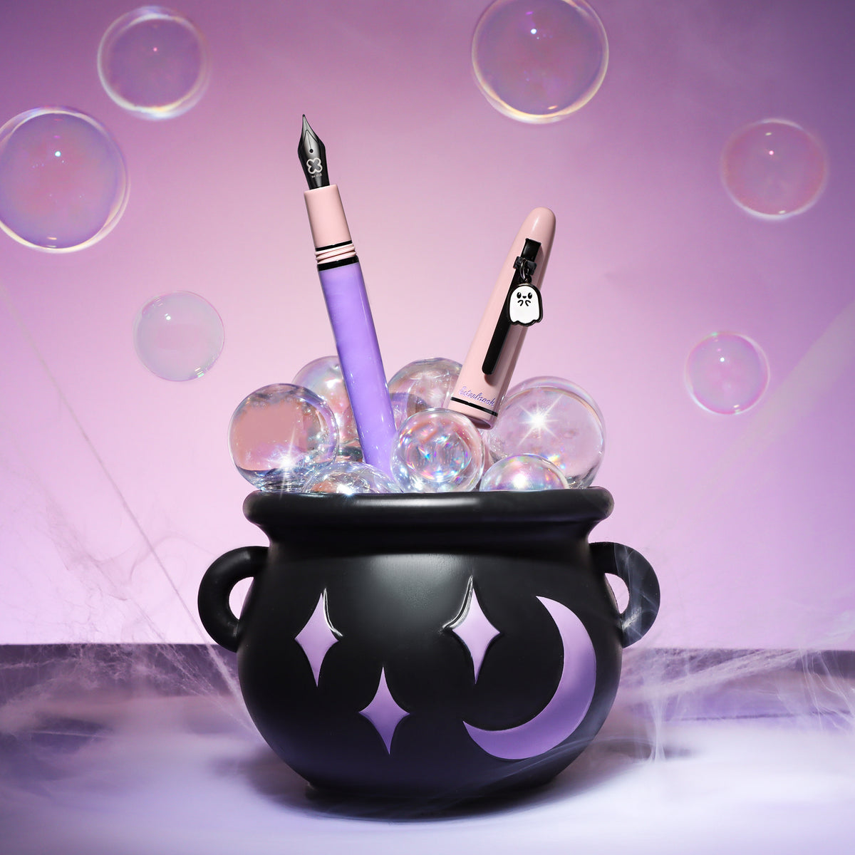 Esterbrook Pastel Halloween Estie fountain pen, purple barrel and pink cap with ghost charm, rising from a black cauldron with bubbles