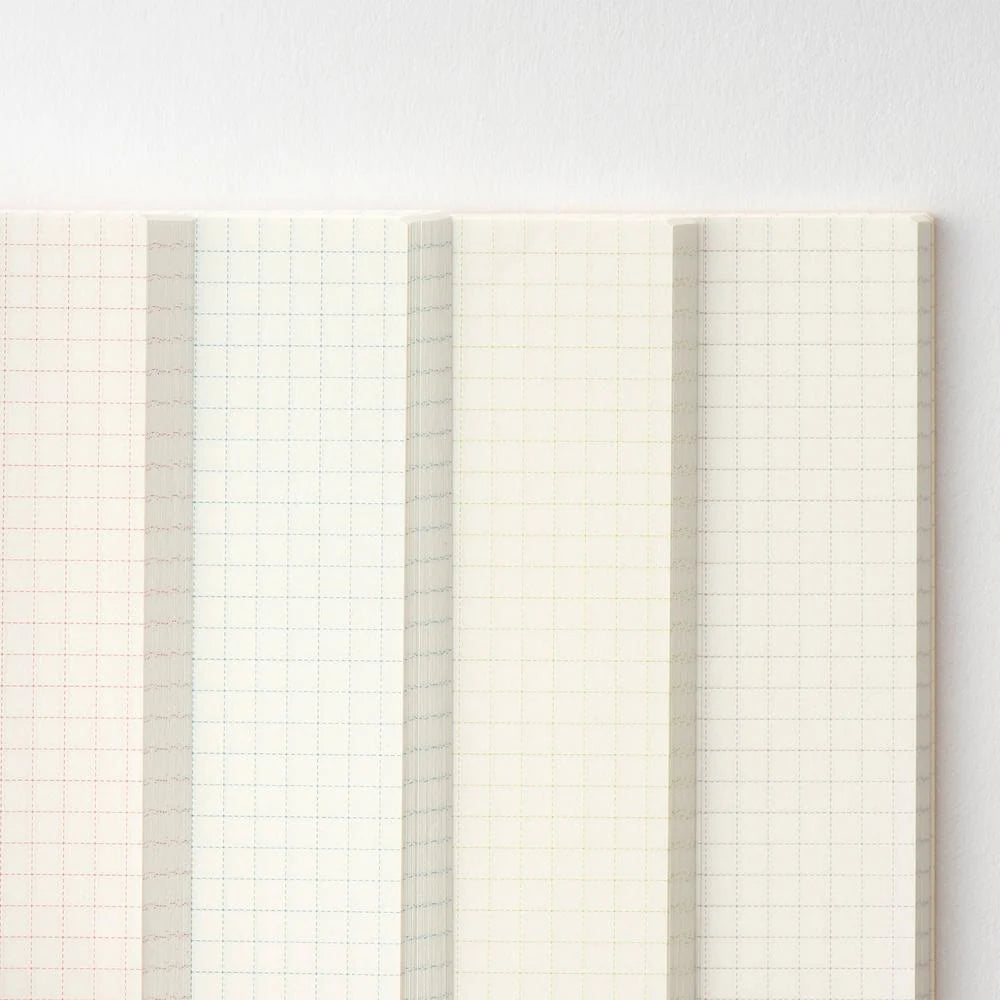 Fanned pages of the Hobonichi A6 graph notebook showing the grid ink changing color between sections — red, blue, green and purple