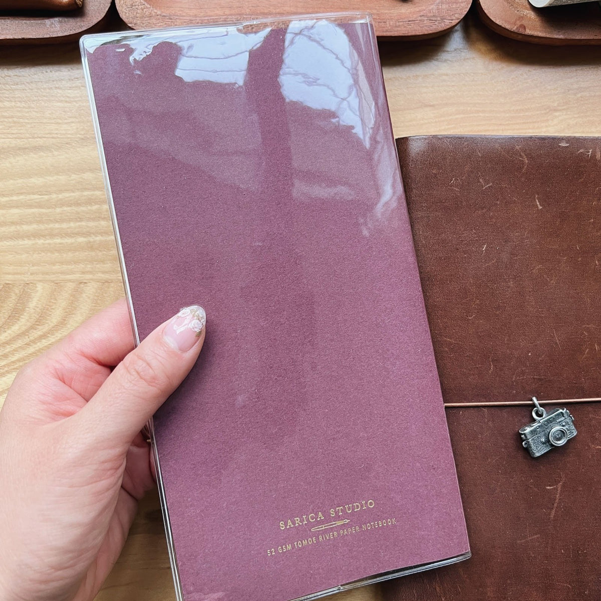 Hand holding a bordeaux Sarica Studio notebook inside the standard size clear cover