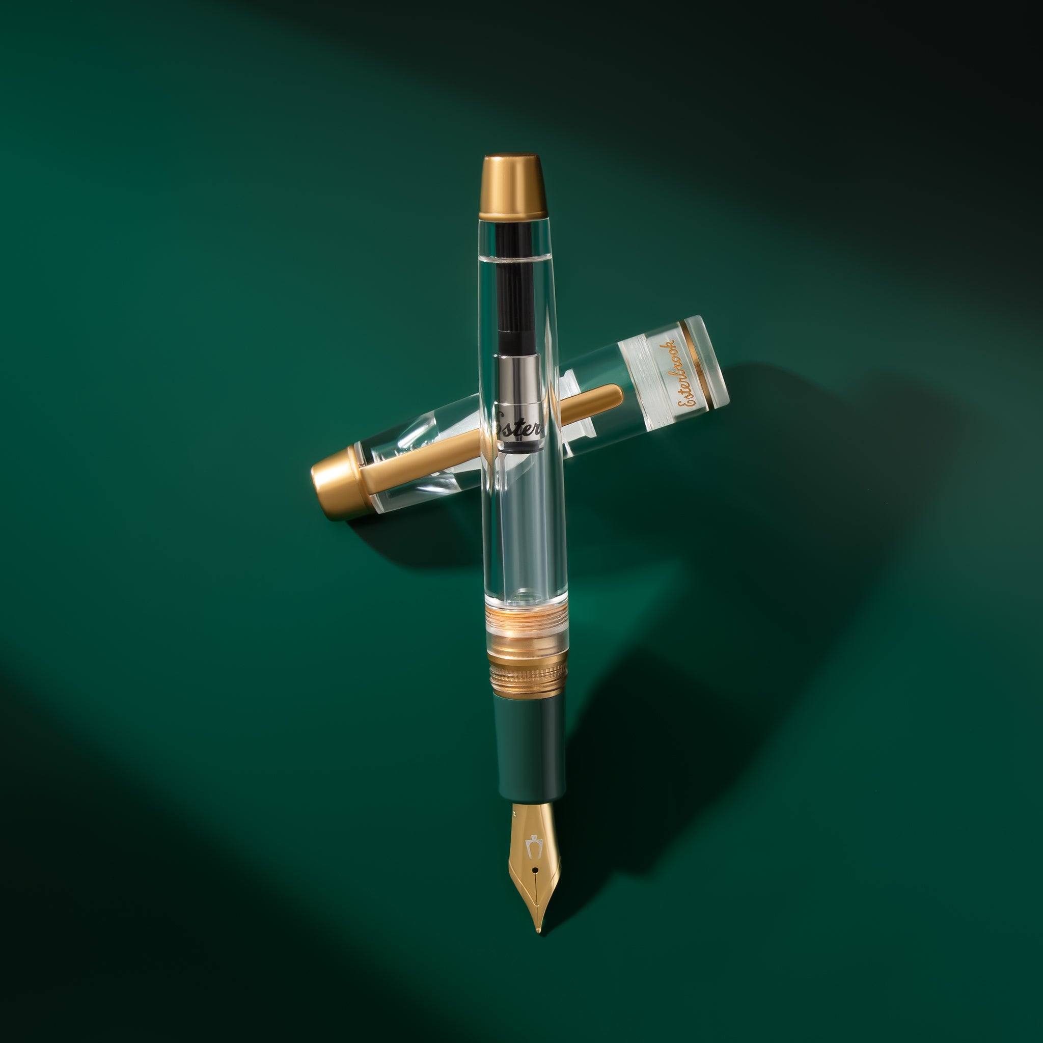 Esterbrook x Accutron Spaceview Estie clear fountain pen with cap off, gold trim and Esterbrook logo, on a green background