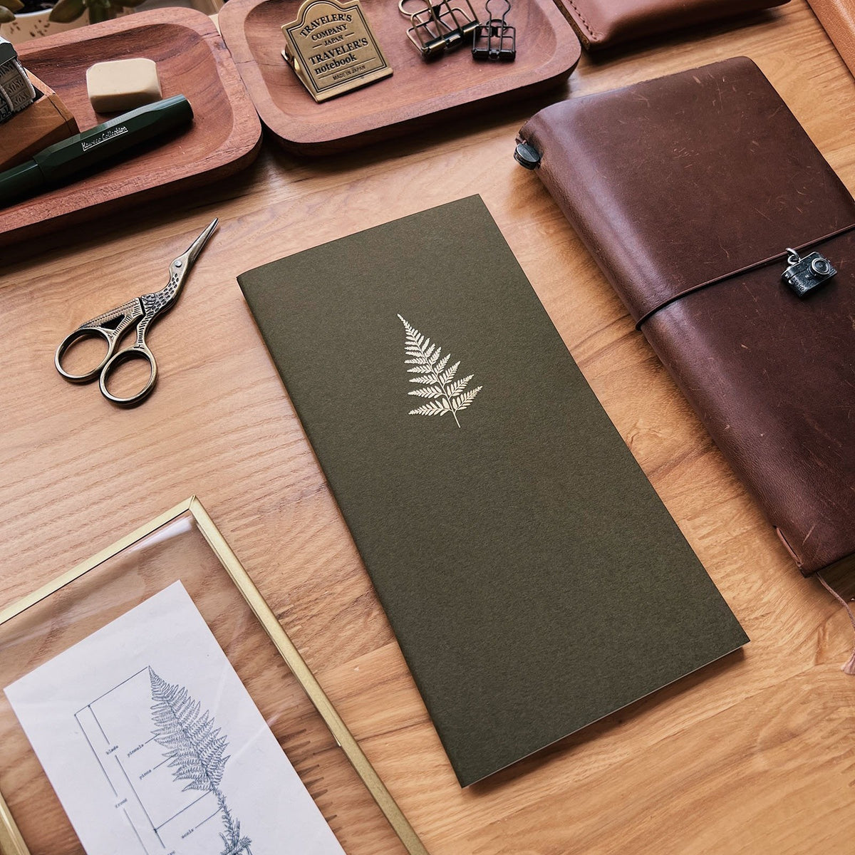 Sarica Studio Fern Notebook, standard TN size, forest green with a gold fern, beside a brown leather traveler's notebook
