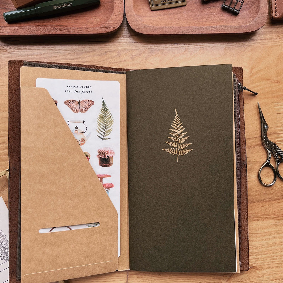 Sarica Studio Fern Notebook, standard TN size, inside a leather traveler's notebook next to a kraft pocket folder