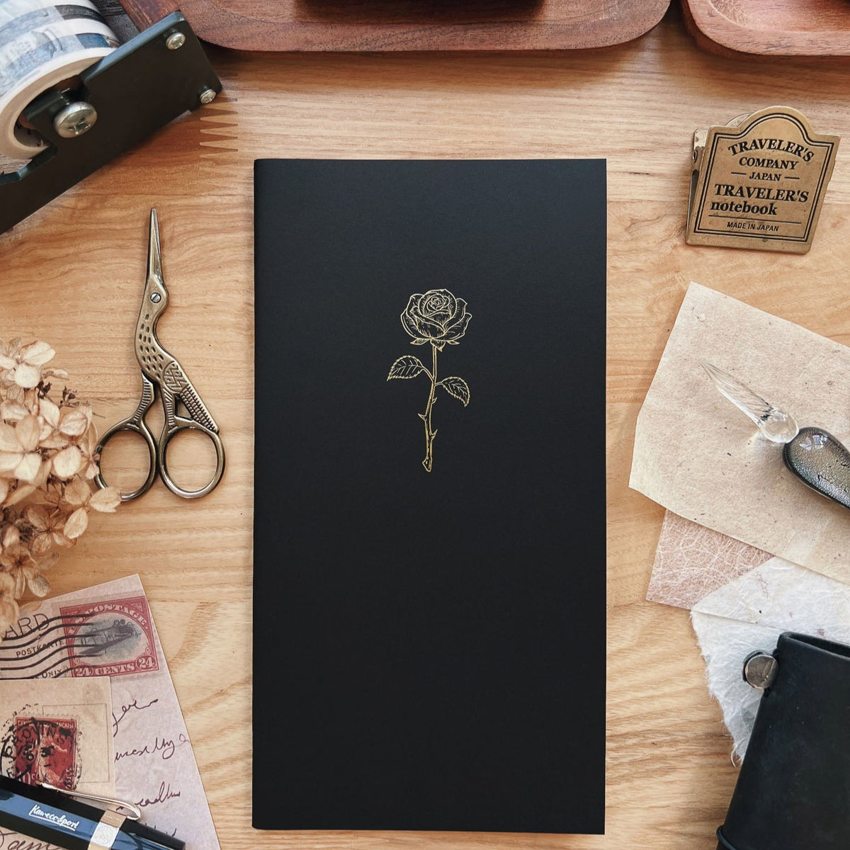 Sarica Studio Rose Notebook, standard TN size, black cover with a gold debossed rose design on a wooden desk