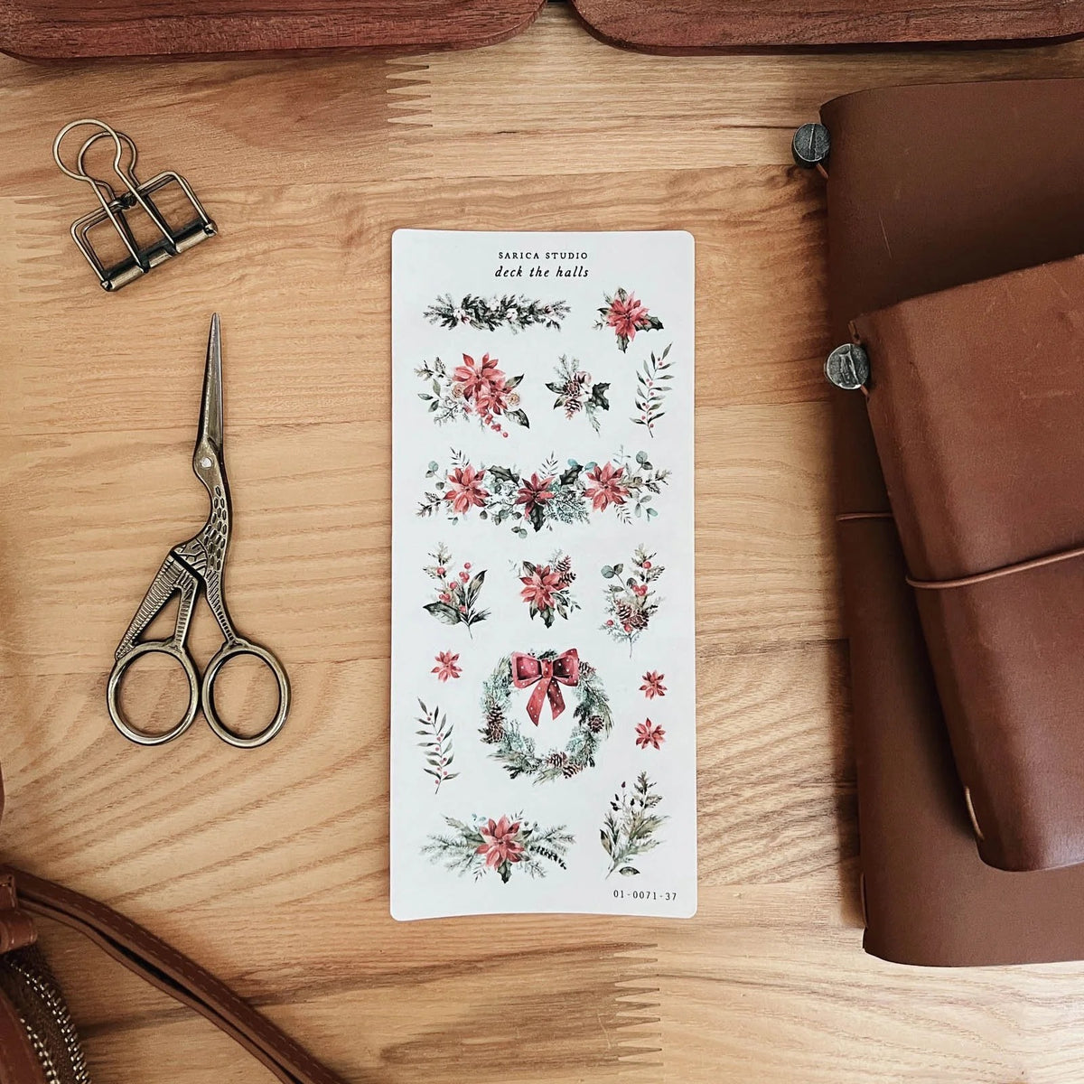 Sarica Studio Deck the Halls sticker sheet of holly, poinsettias and a wreath beside a leather traveler's notebook