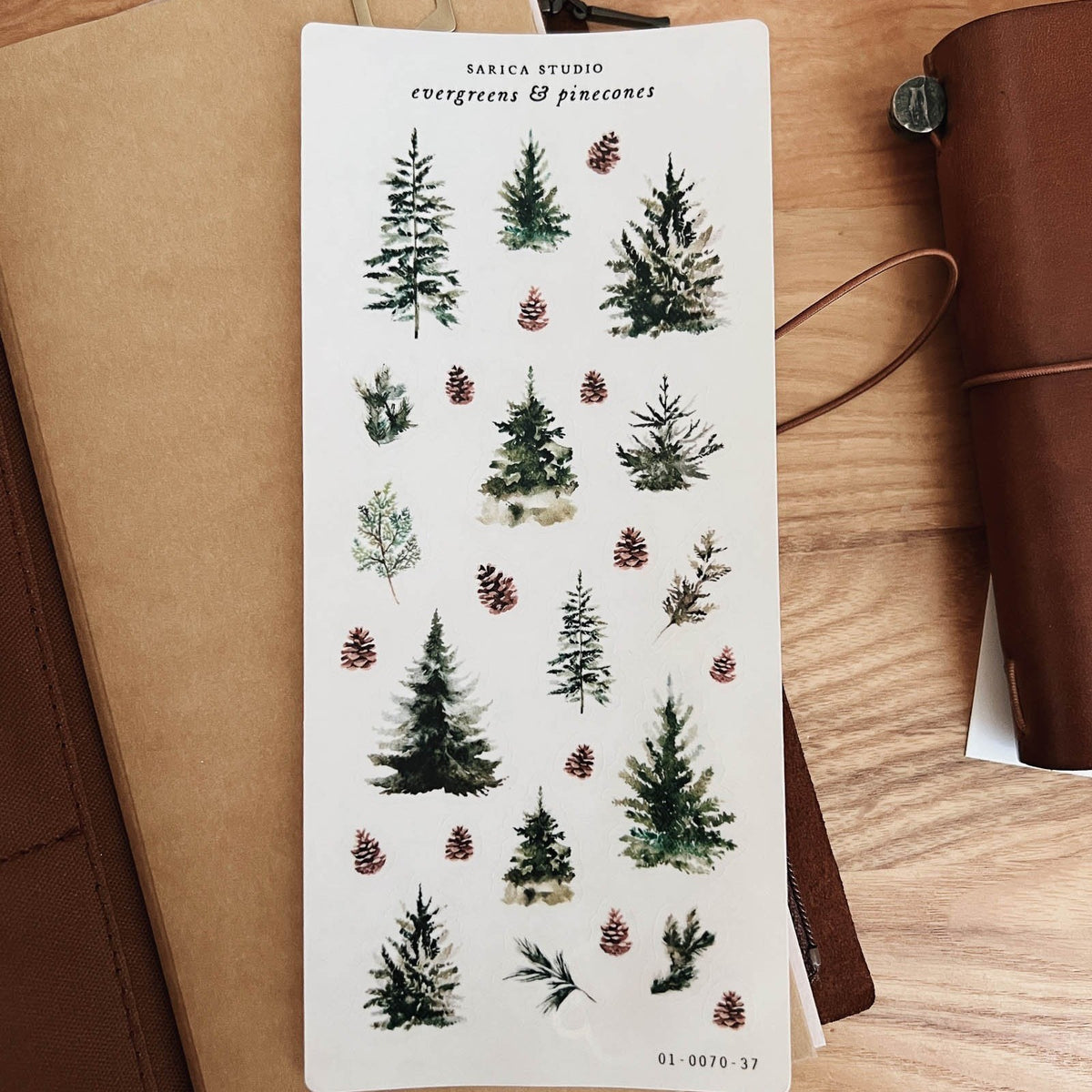 Sarica Studio Evergreens & Pinecones sticker sheet on a brown leather traveler's notebook