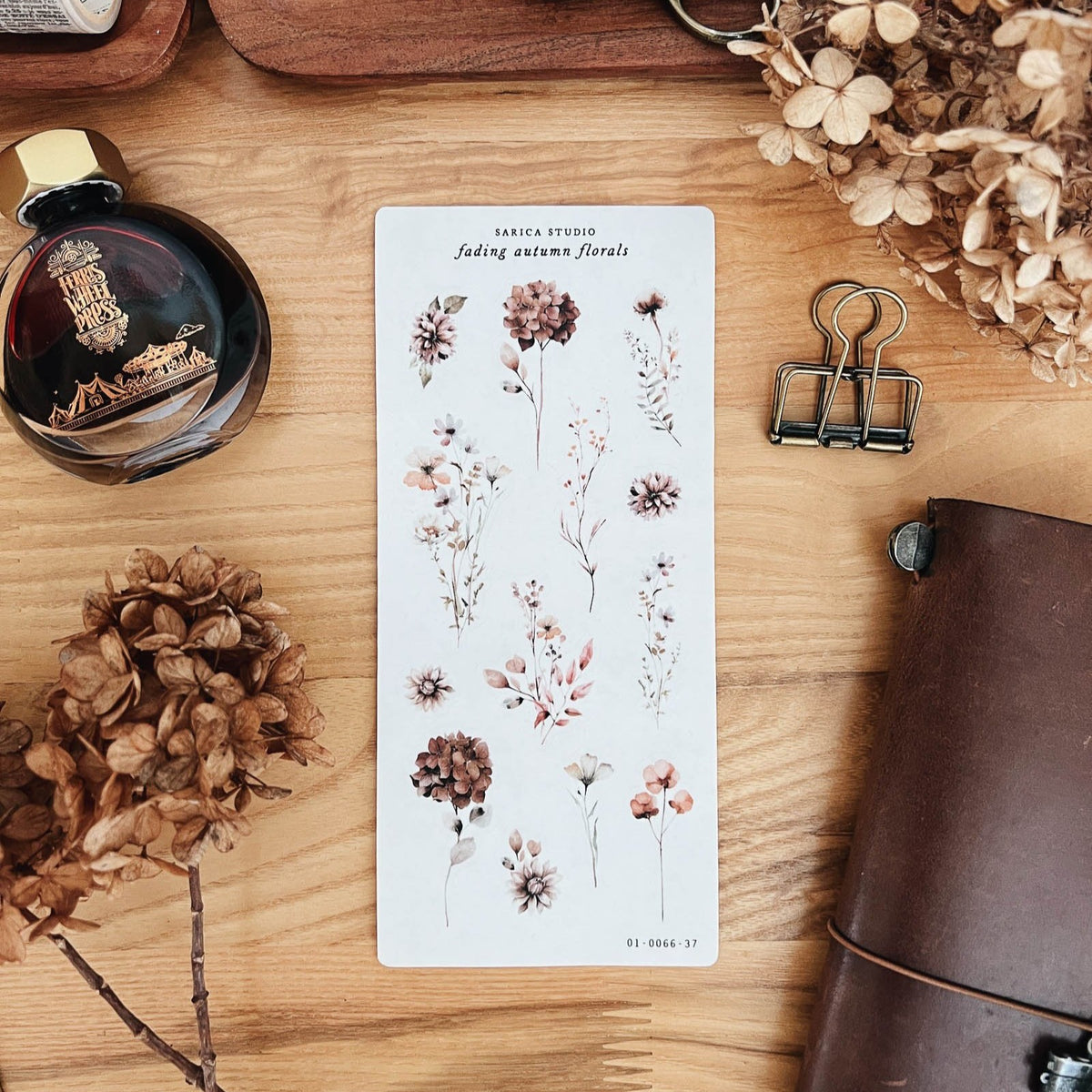 Sarica Studio Fading Autumn Floral sticker sheet of dried flowers in dusty rose and brown, beside dried hydrangeas and a leather traveler's notebook