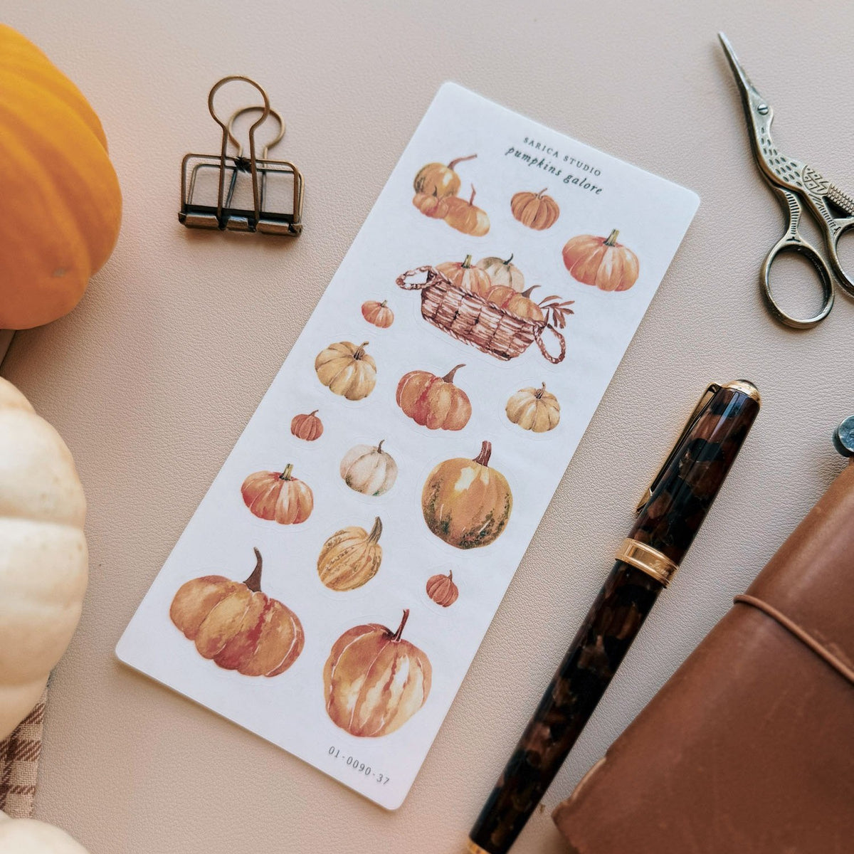 Sarica Studio Pumpkins Galore stickers, sheet shown at an angle beside a white pumpkin