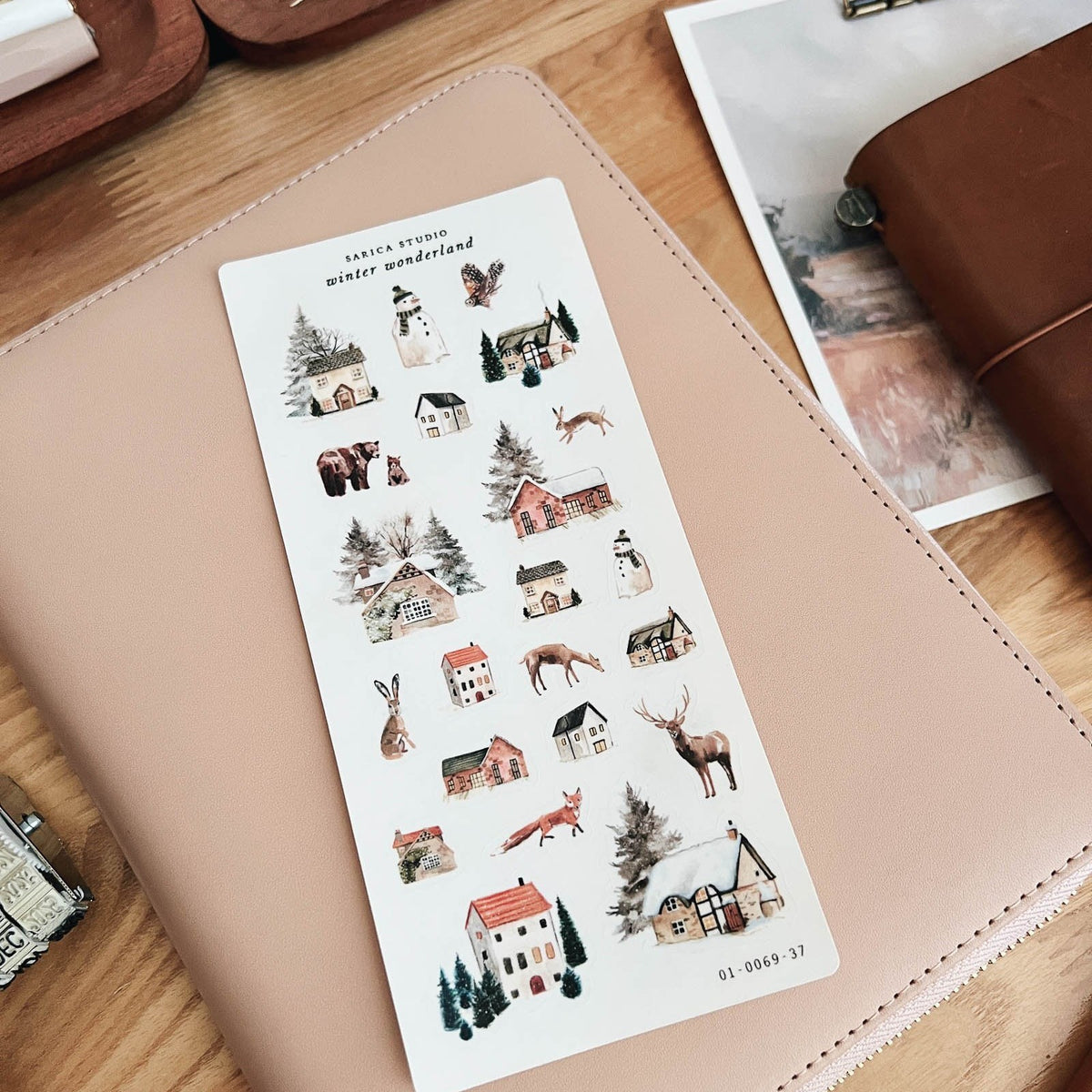 Sarica Studio Winter Wonderland sticker sheet shown at an angle on a blush leather notebook cover