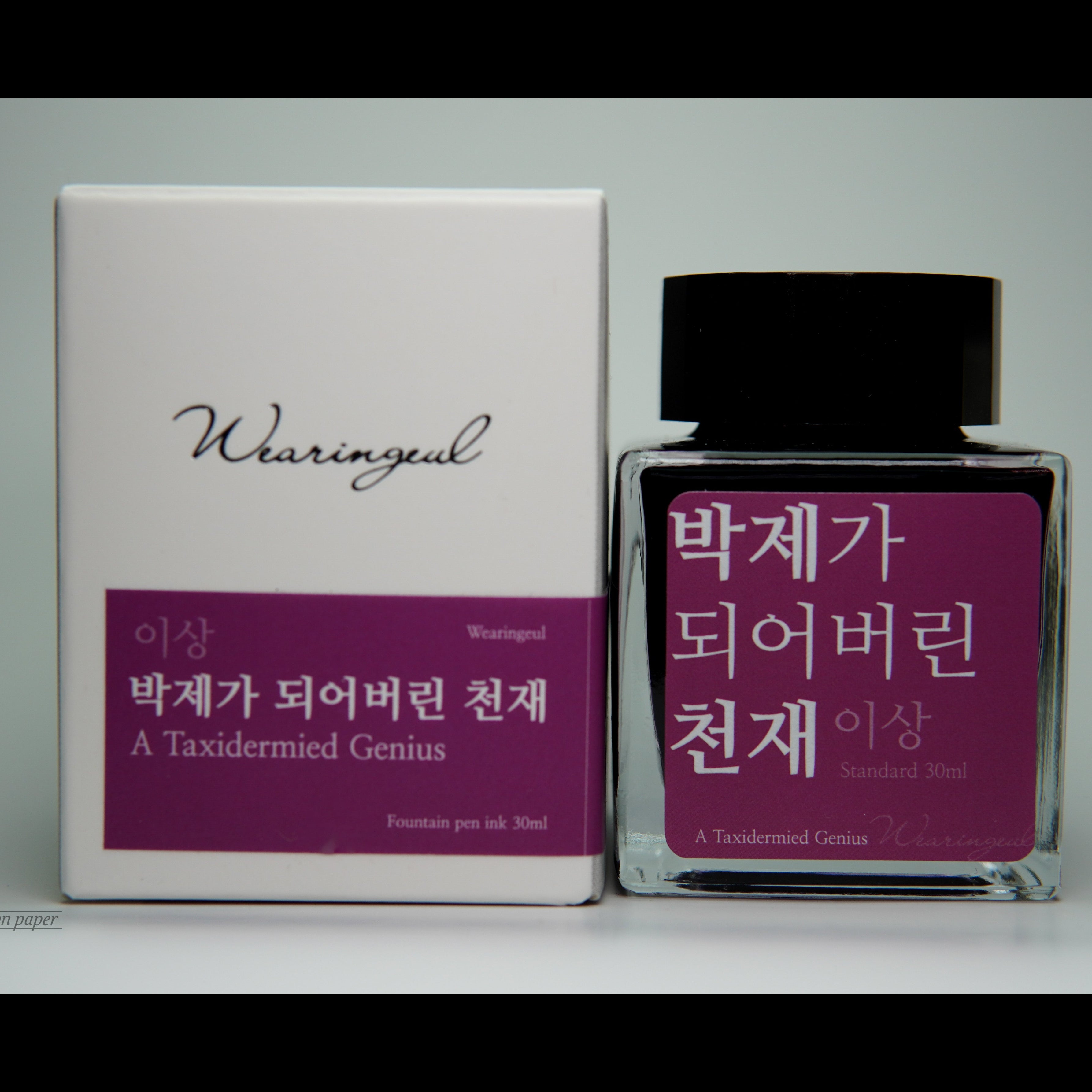 Ink bottle with red label and black cap next to white box with red label