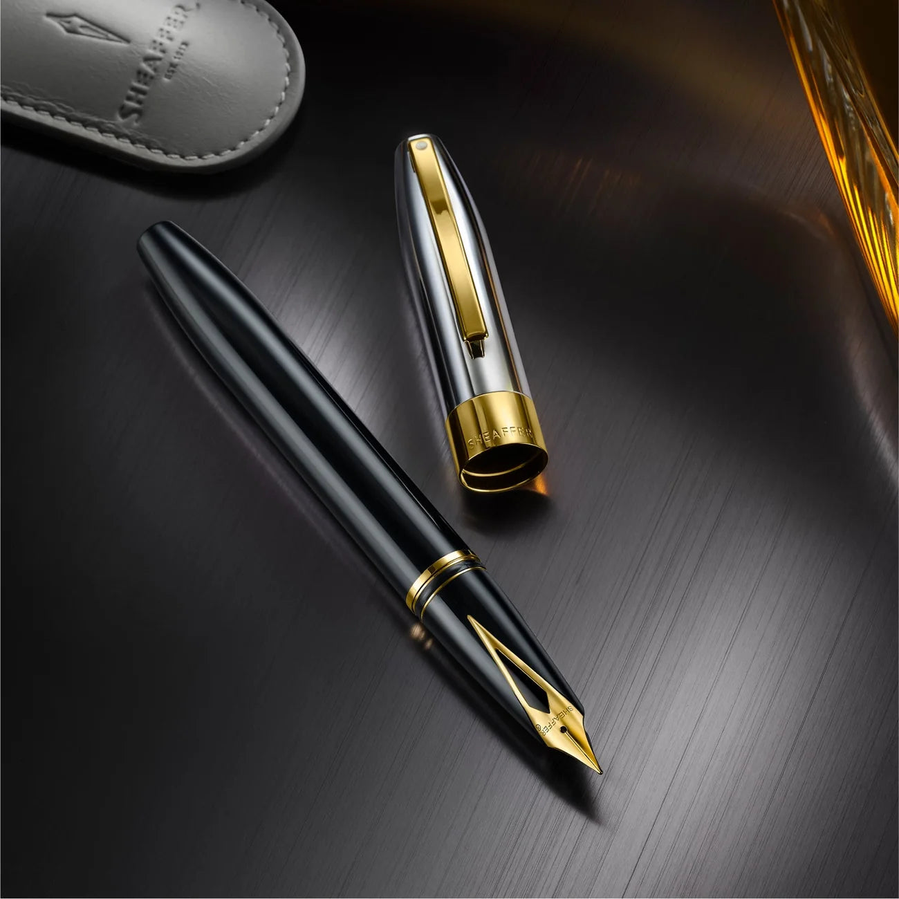 Sheaffer Legacy fountain pen shown capped and uncapped on a dark surface beside its leather pouch, showing the chrome cap and gold trim