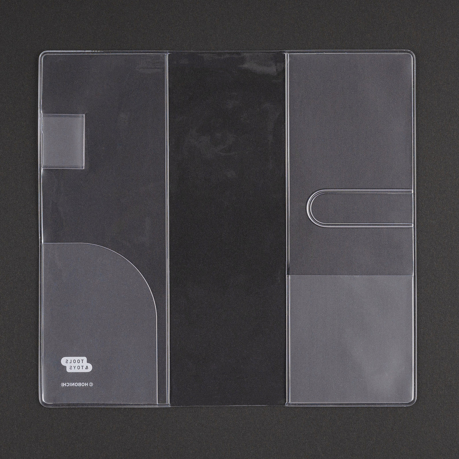 Hobonichi clear cover for the Techo Weeks and Weeks Mega laid flat on a dark surface, showing the inner card pocket, the side flaps and the Hobonichi mark