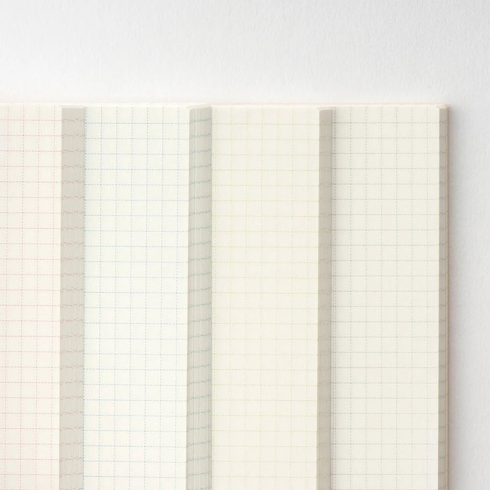 Fanned pages of the Hobonichi A5 graph notebook showing the grid ink changing color between sections — red, blue, green and purple